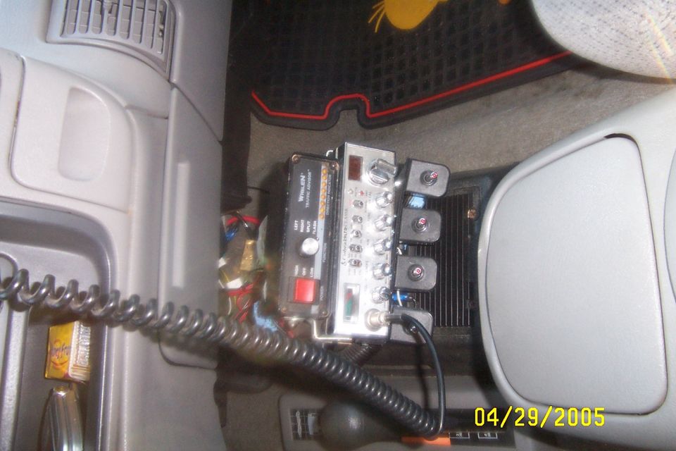 Whelen Traffic Advisor and switch controls mounted on gray vehicle center console with coiled cord.