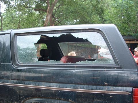 1993 Ford Bronco - Side view of a dark SUV, likely a 1993 Ford Bronco, with its rear window completely shattered.