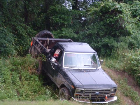 1993 Ford Bronco - A black Ford F-Series pickup truck is partially stuck in the mud on a grassy hill.