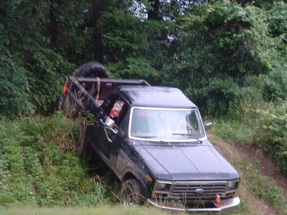 Black Ford F-Series pickup truck stuck on a muddy incline with a spare tire in the bed