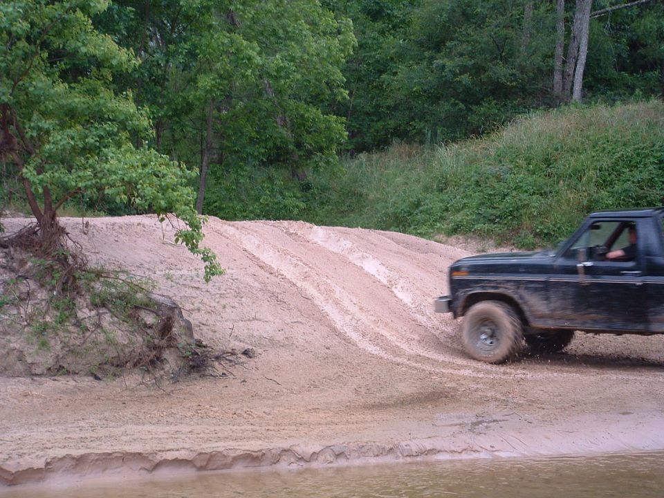 Black 1980s SUV driving on a sandy hill