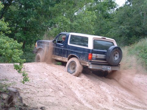 1993 Ford Bronco - A Ford Bronco navigates a dirt hill, its tires spraying mud.