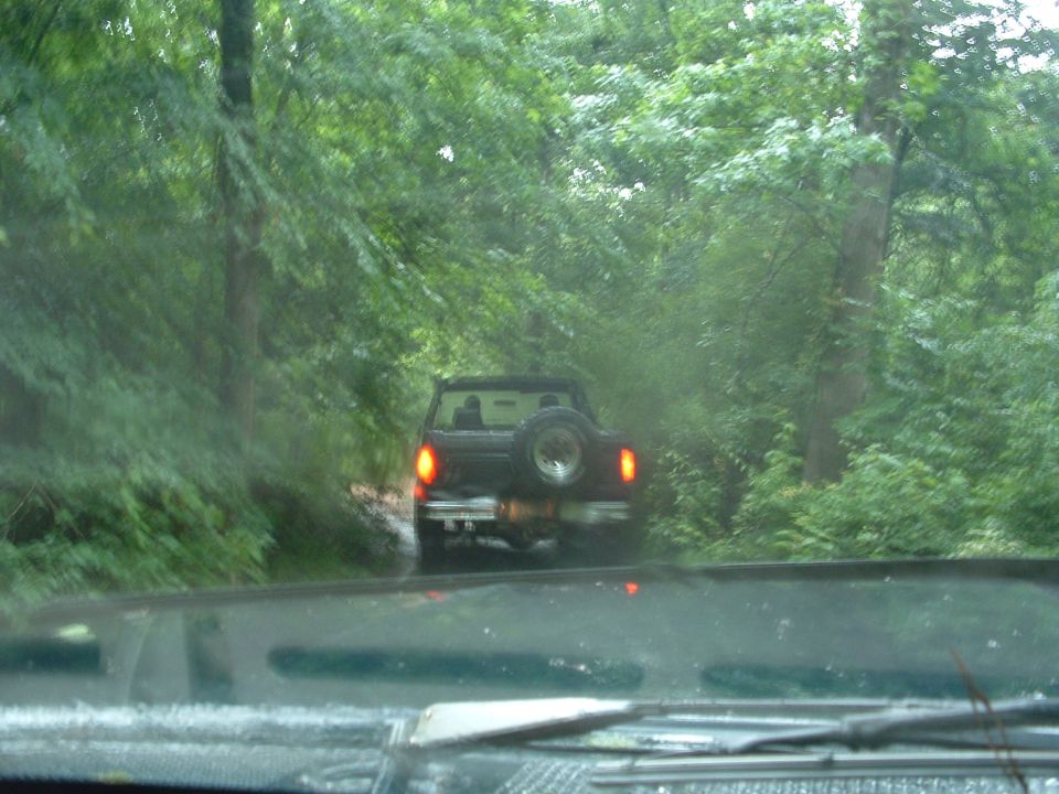 1993 Ford Bronco driving on a dirt road surrounded by trees