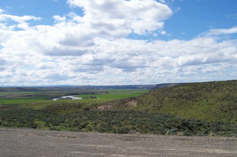 1994 Ford F-150 - A wide landscape view shows a river winding through green fields with hills and mountains in the background under a partly cloudy sky.