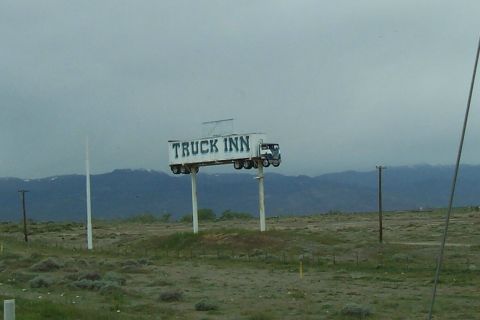 1994 Ford F-150 - A roadside billboard designed to look like a semi-truck is visible against a cloudy sky.