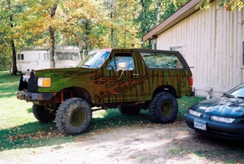 1993 Ford Bronco - A modified Ford Bronco with a custom paint job sits parked next to a house and another car.