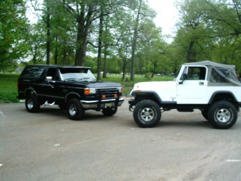 1989 Ford Bronco - Two SUVs, a black 1989 Ford Bronco and a white Jeep Wrangler, are parked side-by-side outdoors.