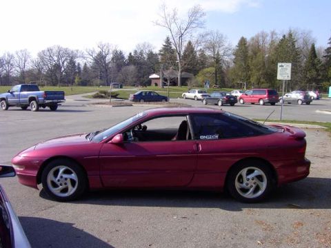 1989 Ford Probe - A red 1989 Ford Probe is parked in a lot, with a blue pickup truck visible in the background.