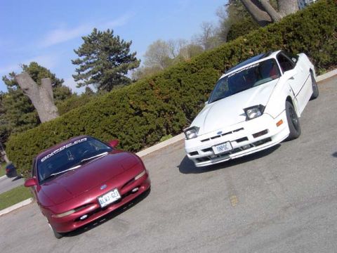1989 Ford Probe - Two Ford Probes, a red one and a white one, are parked outdoors on a sunny day.