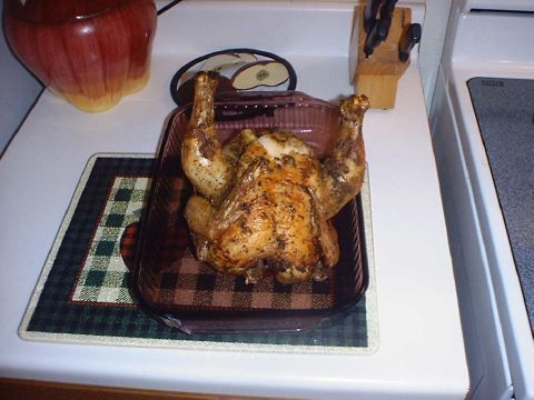 1988 Ford Bronco - A roasted whole chicken sits in a dark roasting pan on a white kitchen range, next to a knife block and an apple-shaped cookie jar. No vehi…