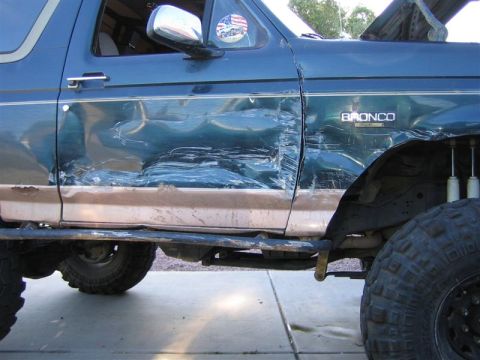 1994 Ford Bronco - The driver's side of a Ford Bronco shows significant body damage, including a crumpled door and fender.