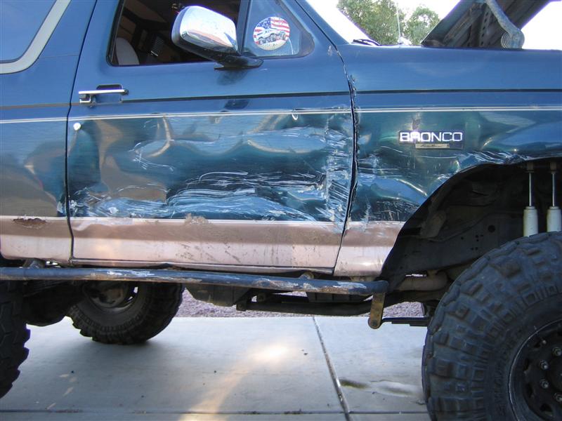 Blue Ford Bronco with heavy crush damage to driver door and quarter panel, BRONCO badge visible