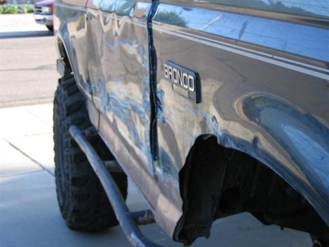 1994 Ford Bronco - This Ford Bronco displays extensive body damage on its side, with a creased door and dented quarter panel.