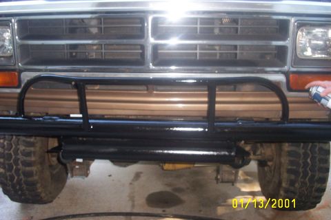 1979 Ford F-150 - A person sprays black paint onto a custom front bumper installed on a vehicle. The grille and headlights are visible above the bumper.