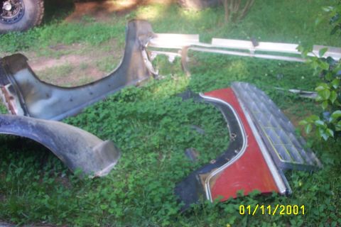 1979 Ford F-150 - Scattered car parts, including a fender and a grille section, lie on a grassy area.