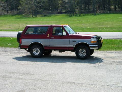 1995 Ford Bronco - This two-tone Ford Bronco is parked on a gravel surface with a grassy hill in the background.
