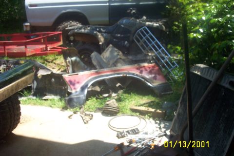 1979 Ford F-150 - A collection of vehicle parts and an ATV are piled up outdoors next to a white truck.