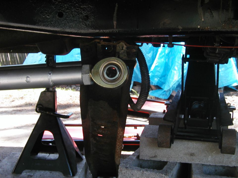 Close-up of a vehicle's suspension linkage with a heim joint, supported by jack stands and blocks