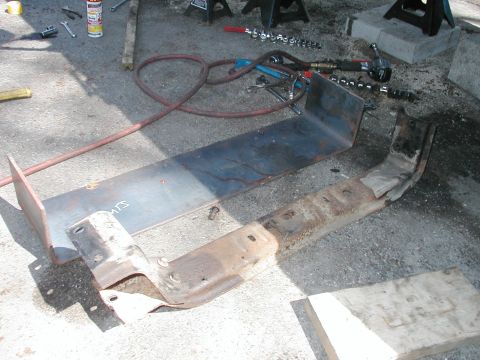 1994 Ford Bronco - Two metal components, possibly from a vehicle's frame or suspension, lie on the ground next to various tools.