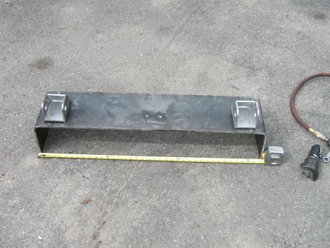 1994 Ford Bronco - A metal bracket with mounting tabs is measured on asphalt next to an air hose fitting.