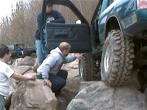 1977 Ford F-150 - People are gathered around two trucks navigating a rocky terrain, with one truck's large tire prominently displayed.