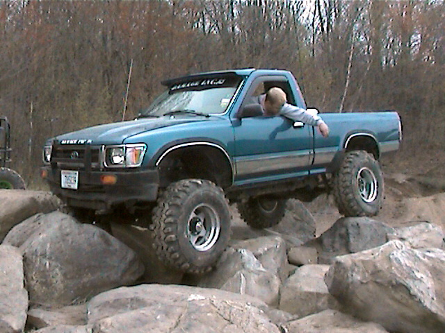Blue pickup truck with large tires navigating a rocky obstacle course