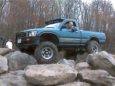 1977 Ford F-150 - A man drives a lifted teal pickup truck over a rocky obstacle course.