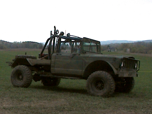 Olive drab military truck with roll cage and large off-road tires parked on grass