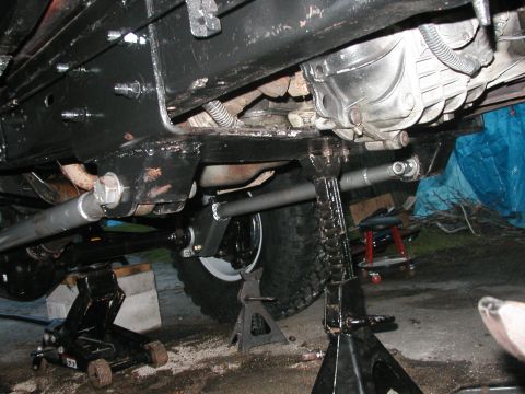 1994 Ford Bronco - The underside of a vehicle is shown, lifted by multiple jack stands and a floor jack for maintenance.