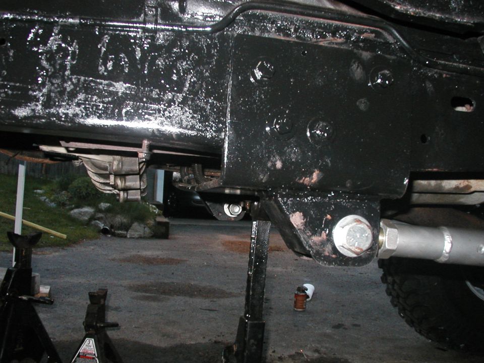 Underside of a vehicle on jack stands, showing frame, suspension, and drivetrain parts