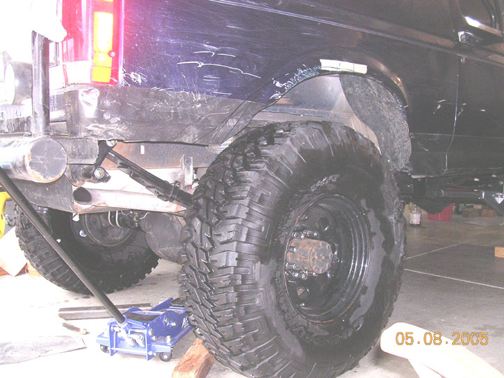 Trimmed rear fender opening and mud-terrain tire on a dark blue Ford Bronco in a garage