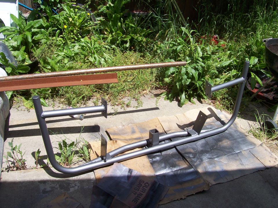 Gray-primered tubular bumper on cardboard outdoors next to garden bed