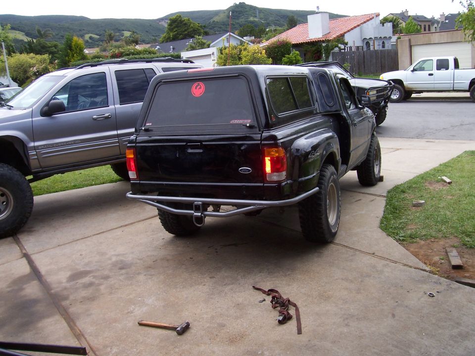 Three-quarter rear view of black Ford pickup with shell and tube bumper, hills behind