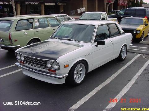 1986 Ford Bronco - A white Datsun 510 sedan is parked in a lot with other vehicles visible.