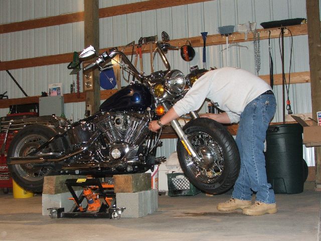 Person working on the front end of a blue cruiser raised on a scissor lift