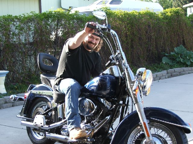 Man seated on a dark blue Harley-Davidson Softail on a driveway, right side view