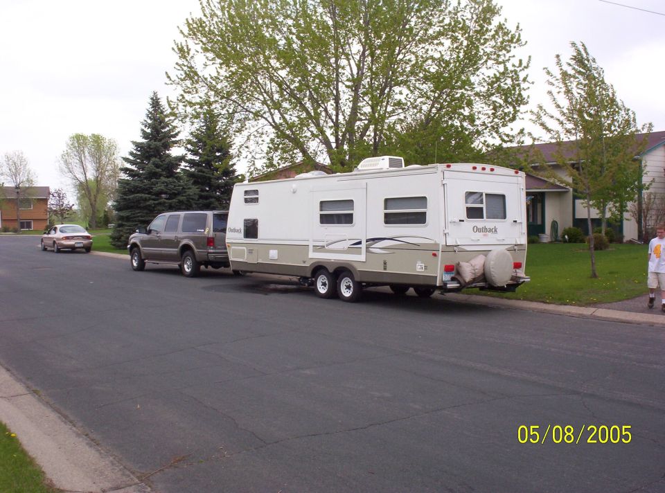 Brown Ford Excursion towing a white and tan travel trailer on a residential street