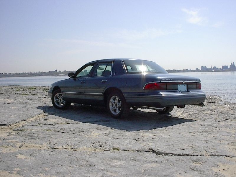 Blue-gray Mercury Grand Marquis LS sedan rear 3/4 view on rock with skyline behind