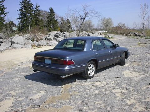 1985 Mercury Grand Marquis - A dark blue sedan is parked on a rocky surface under a clear sky.