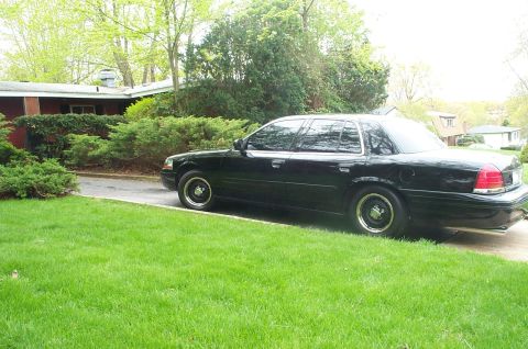 1999 Ford Crown Victoria - Black Ford Crown Victoria sedan parked in a residential driveway, seen from the passenger side and slightly rear, with tinted windows, blac…