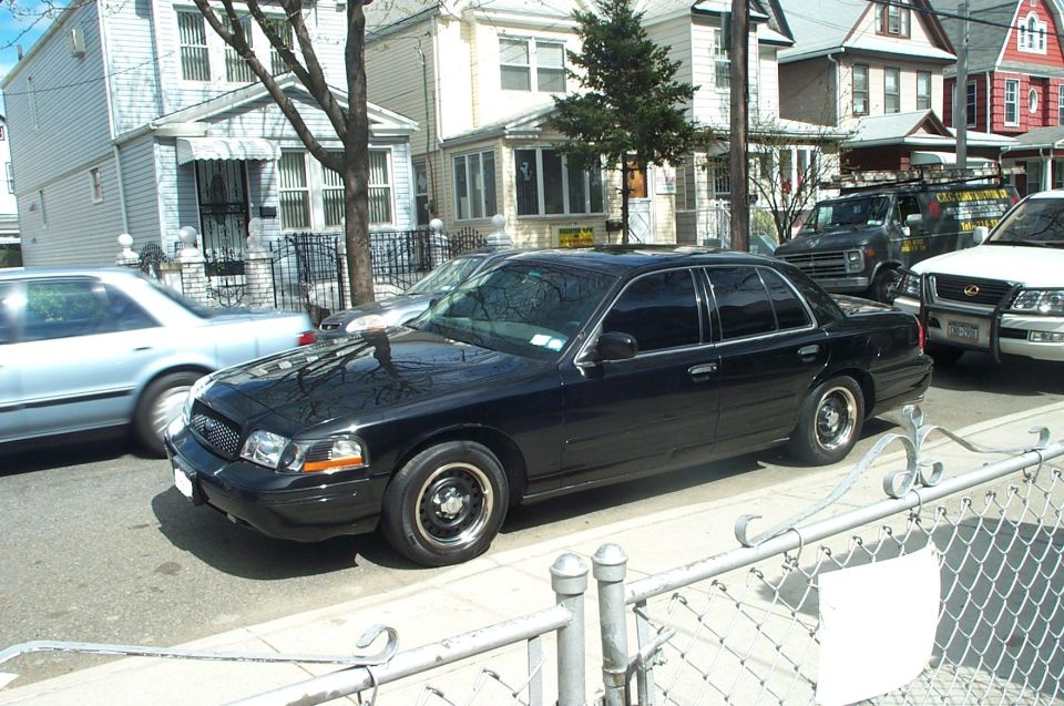 Black Ford Crown Victoria sedan at curb with steel wheels and tinted windows