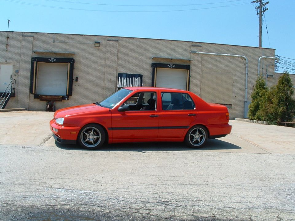 Red sedan parked on concrete in front of a brick building with loading docks
