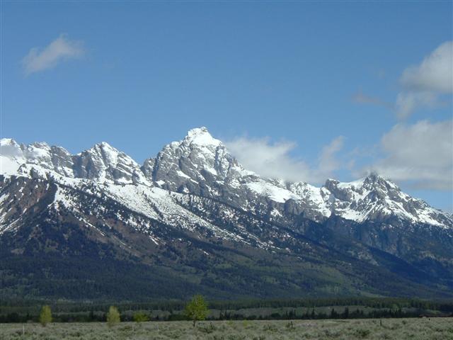 Snow-capped mountain range with sagebrush flats in foreground under partly cloudy sky
