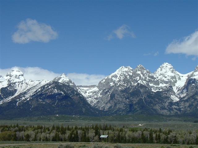 Snow-dusted mountain range above a dark evergreen forest and broad valley floor