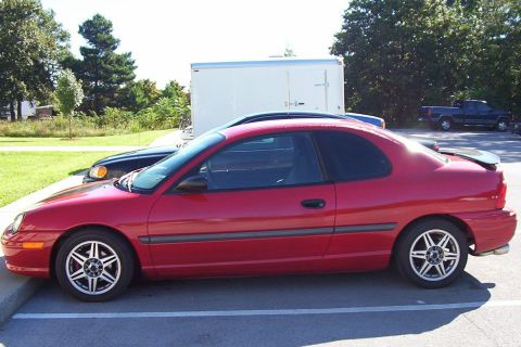 1997 Ford Taurus - Side view of a red coupe parked in a lot with other vehicles and a trailer.