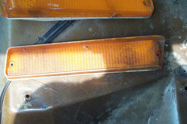 Two faded amber turn signal light lenses lying on a rusty brown metal panel
