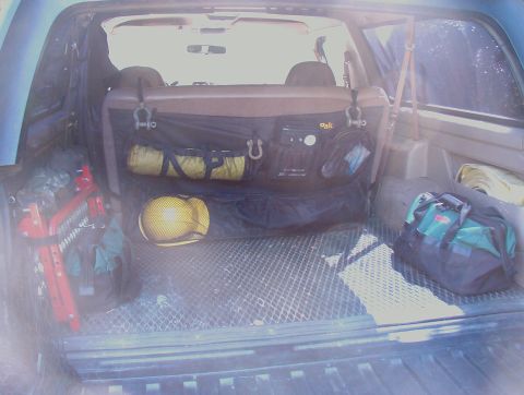 1993 Ford Bronco - The cargo area of a vehicle contains camping gear, including a yellow hard hat and a green and black duffel bag.