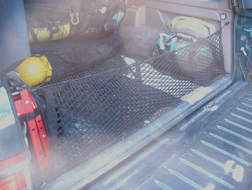 SUV cargo area with black cargo net, red jack and gear bags, tailgate down
