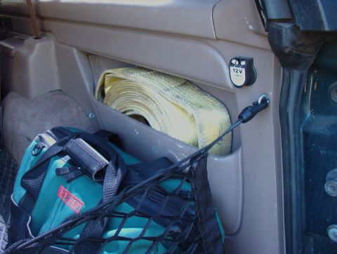 1993 Ford Bronco - The interior of a vehicle shows a storage area with a 12V power outlet and various items.