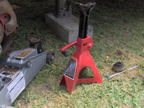 1979 Ford Bronco - A red jack stand and a grey floor jack are positioned on the grass, suggesting vehicle maintenance.